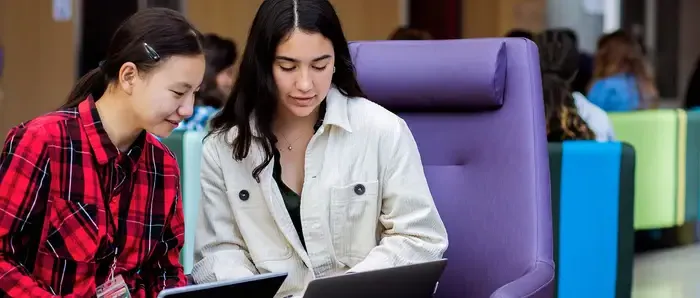 Two Carnegie Mellon students sitting in Tepper Quad, working on their laptops.